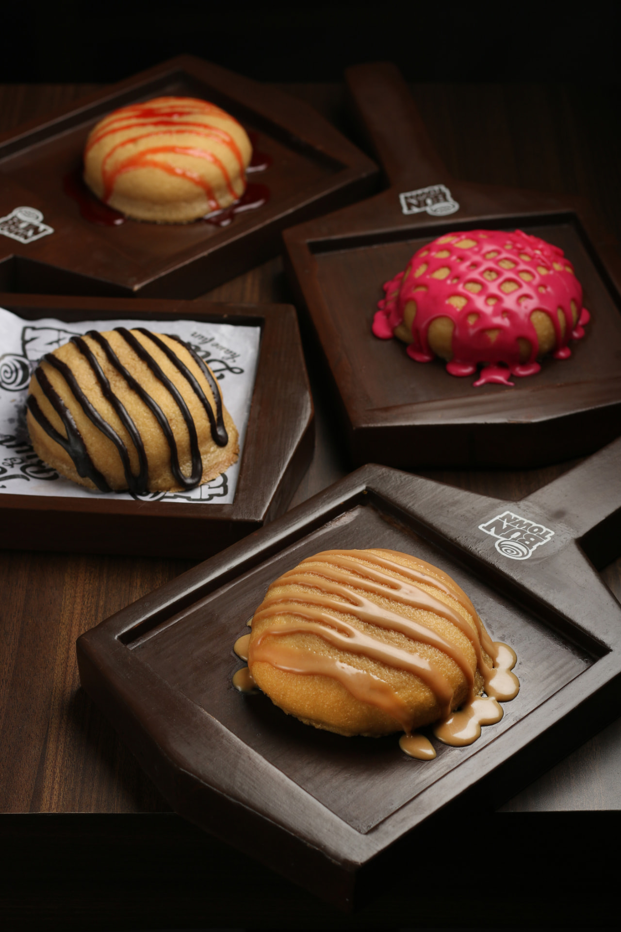 Assorted stuffed buns with chocolate, caramel and berry glazes on wooden boards