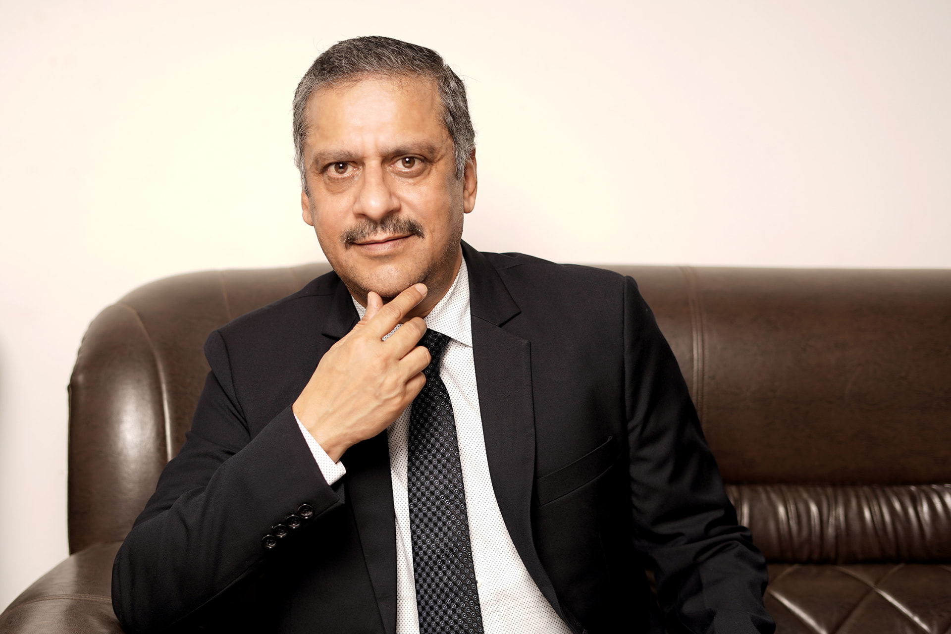 Seated corporate portrait of a senior business leader in a black suit and patterned tie