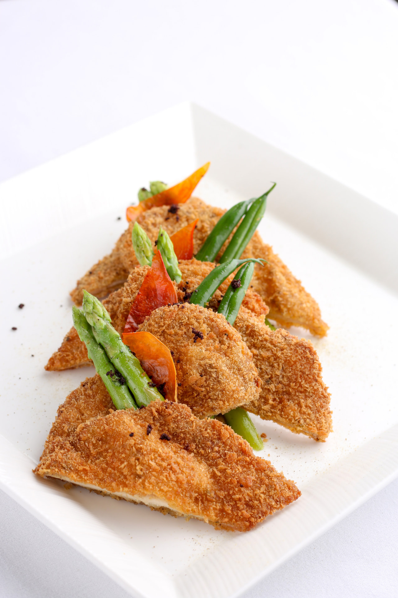 Crumb-fried fish fillets plated with asparagus on a white square plate
