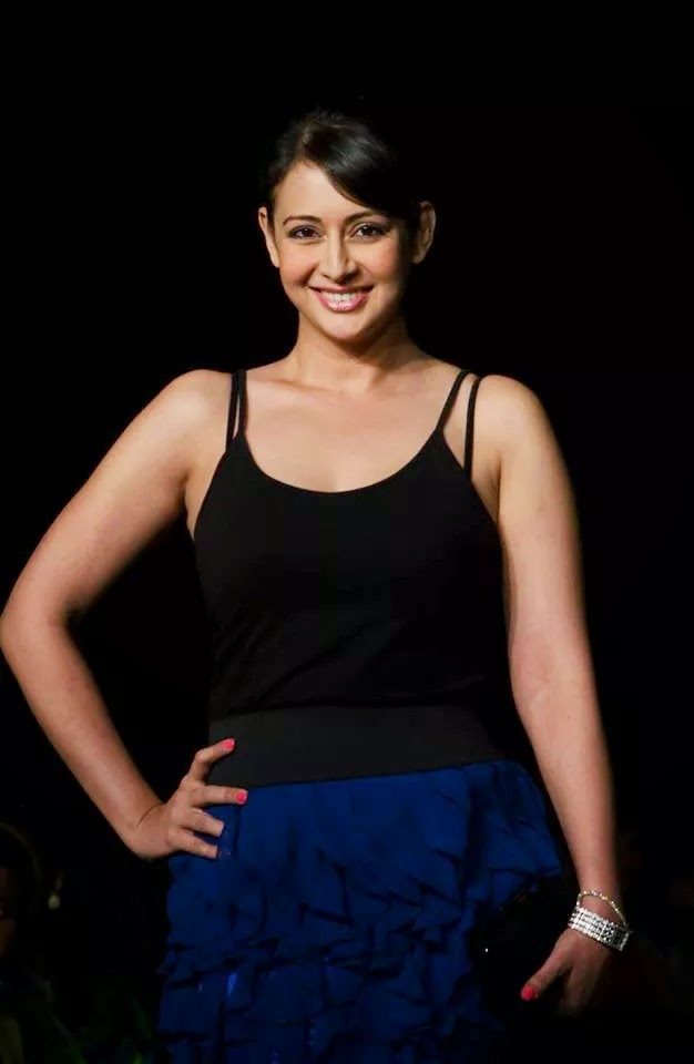 Model walking the ramp in a black top and layered blue ruffled skirt during a fashion show