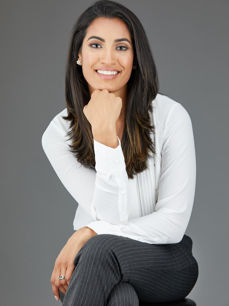 Seated corporate portrait of a businesswoman in a white shirt against a grey studio backdrop