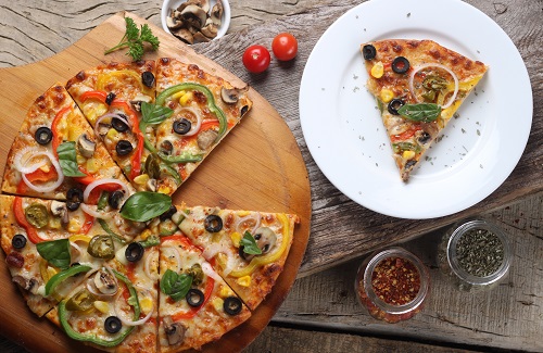 Overhead shot of a vegetable pizza on a wooden board with herbs and chilli flakes